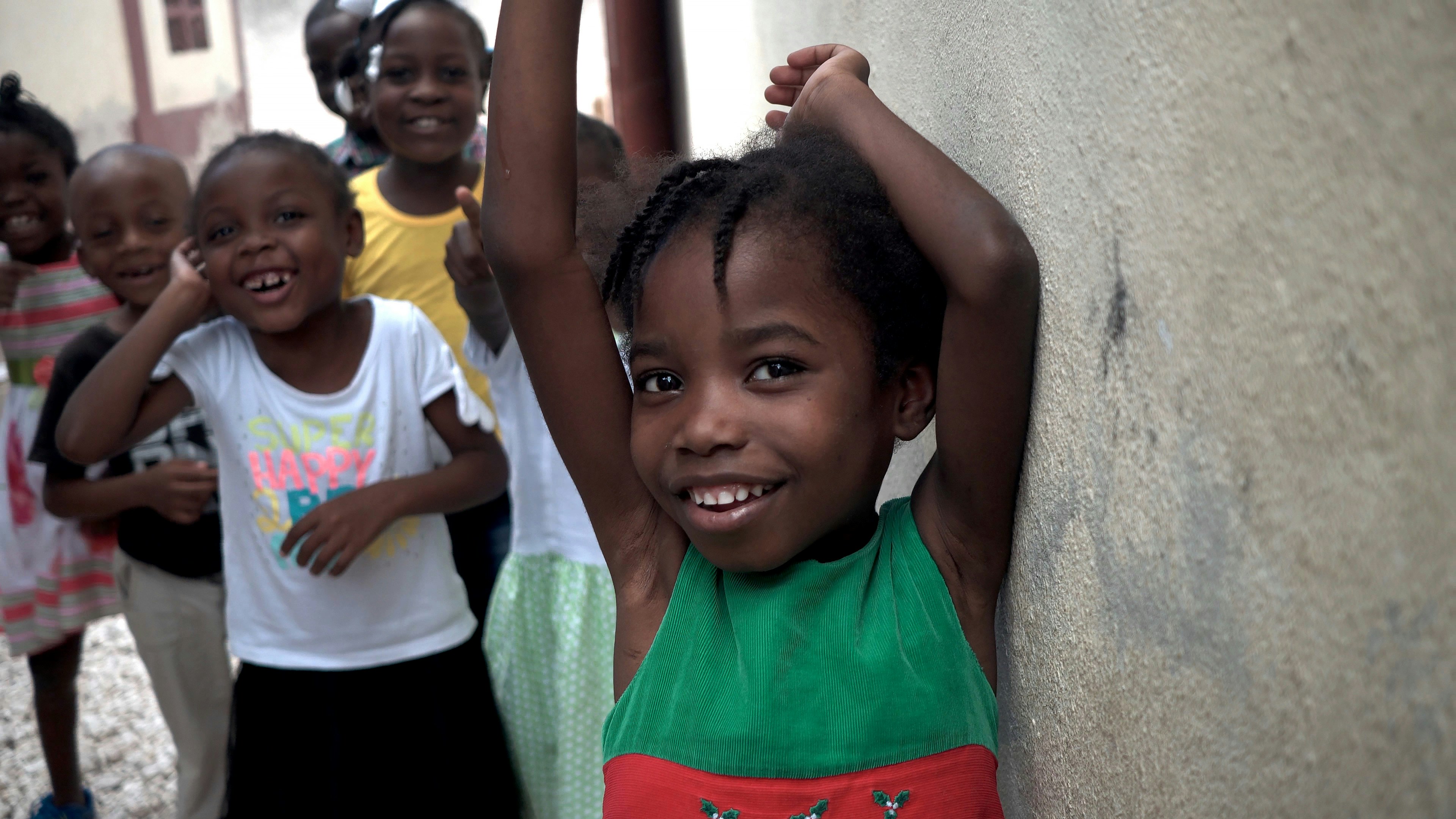 A smiling child leaning against a wall.